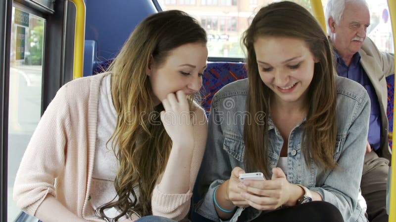 Duas jovens mulheres que leem a mensagem de texto no ônibus