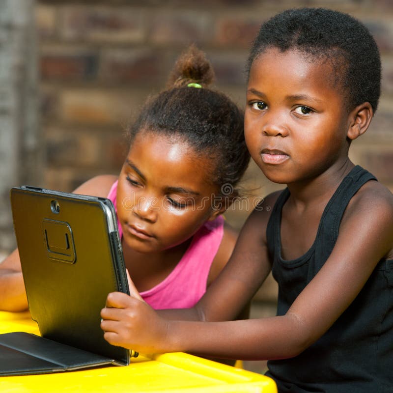 Duas meninas africanas que sentam-se na tabela com tabuleta. imagens de stock Duas meninas africanas que sentam-se na tabela com tabuleta. imagens de stock