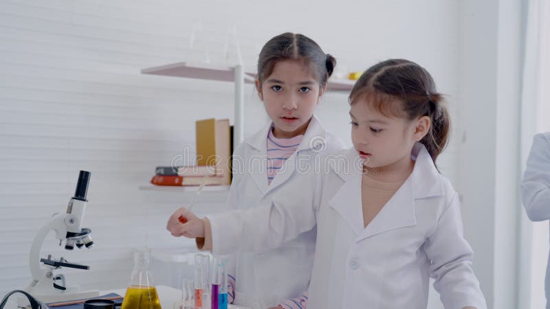 Duas meninas asiáticas 4k desfrutam de um tubo de teste de ciência colorido com amigos dentro da sala de ciência branca de uma esc