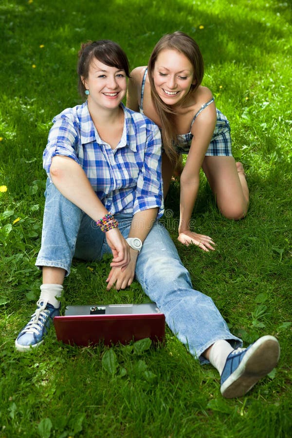 Duas meninas atrativas com um portátil no parque foto de stock Duas meninas atrativas com um portátil no parque foto de stock