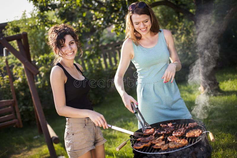 Duas meninas bonitas que fazem o alimento na grade imagem de stock royalty free Duas meninas bonitas que fazem o alimento na grade imagem de stock royalty free
