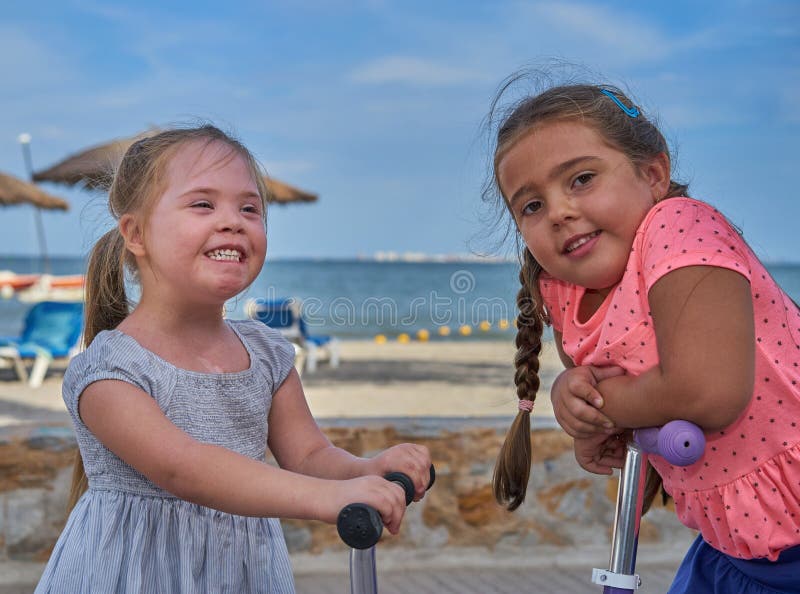 Duas meninas de sorriso em 'trotinette's pela praia imagem de stock Duas meninas de sorriso em 'trotinette's pela praia imagem de stock