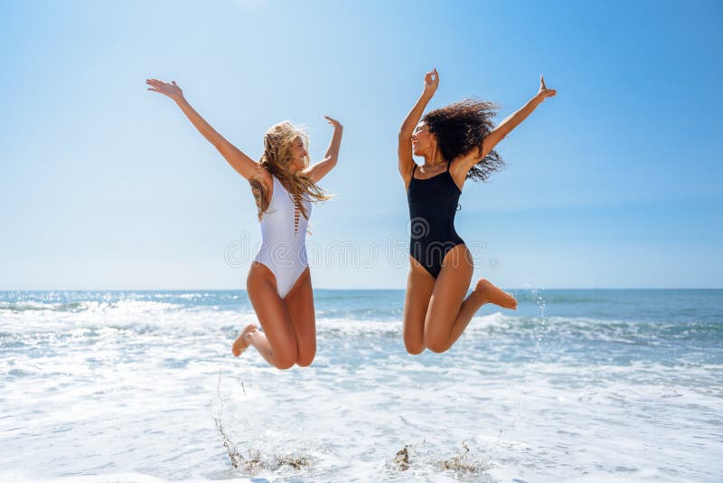 Duas meninas engraçadas no roupa de banho que salta em uma praia tropical imagens de stock Duas meninas engraçadas no roupa de banho que salta em uma praia tropical imagens de stock