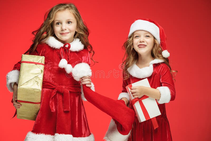 Duas meninas felizes em chapéus de Papai Noel com as caixas de presente no estúdio foto de stock Duas meninas felizes em chapéus de Papai Noel com as caixas de presente no estúdio foto de stock