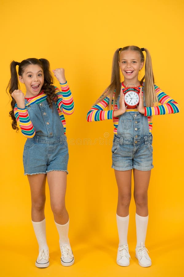 Duas meninas felizes seguram o despertador de volta à escola verão disciplina e gerenciamento de tempo parede amarela das adolesc