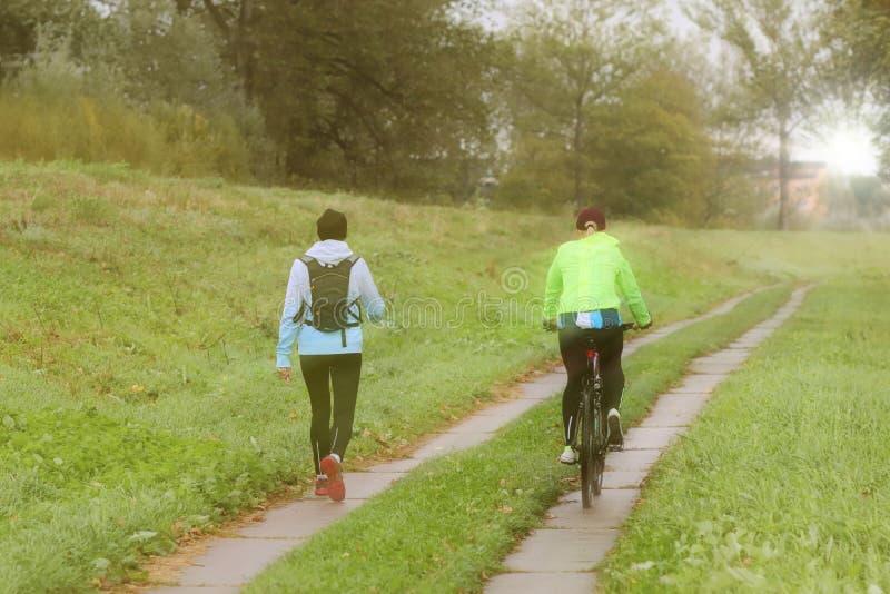 Duas meninas jogam esportes no tempo da manhã ensolarada Ciclagem e passeio sob gotas da chuva no tempo ensolarado Esporte e life imagens de stock Duas meninas jogam esportes no tempo da manhã ensolarada Ciclagem e passeio sob gotas da chuva no tempo ensolarado Esporte e life imagens de stock