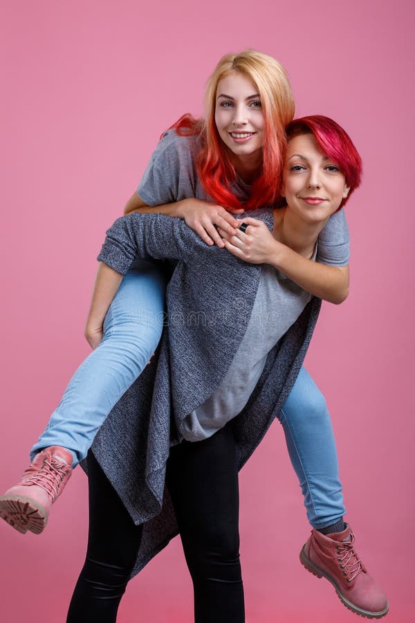 Duas meninas lésbicas, uma aumentaram outra na parte traseira Em um fundo cor-de-rosa fotos de stock Duas meninas lésbicas, uma aumentaram outra na parte traseira Em um fundo cor-de-rosa fotos de stock