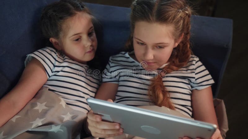 Duas Meninas No Sofá à Noite Com Um Tablet Digital. Jogos Online