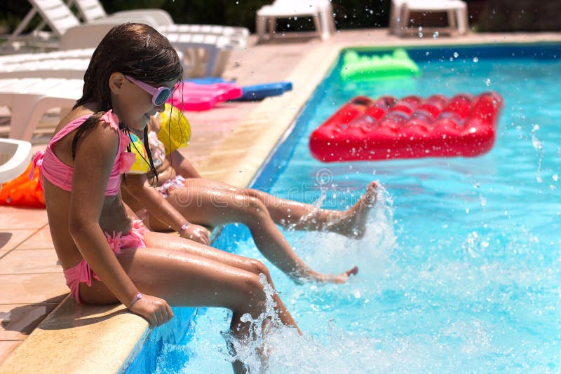Duas meninas sentadas no poolside, tocando, lavando água; fundo de verão imagem de stock royalty free Duas meninas sentadas no poolside, tocando, lavando água; fundo de verão imagem de stock royalty free