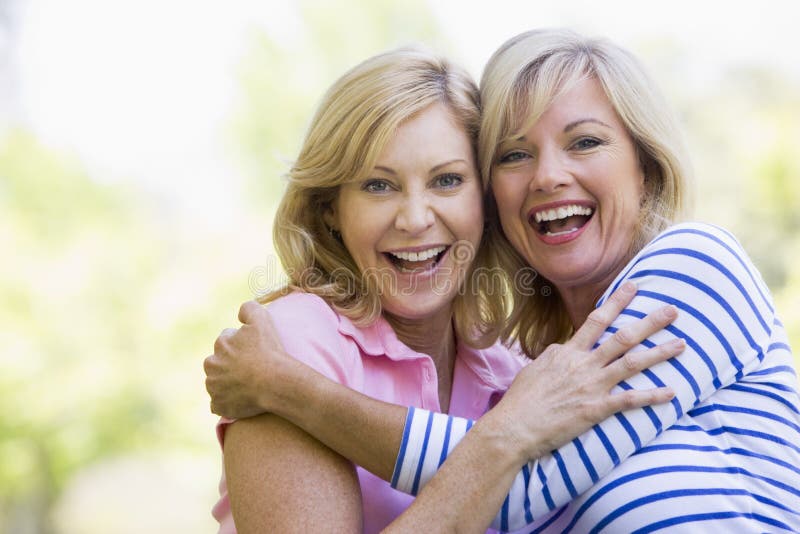Duas mulheres ao ar livre que abraçam e que sorriem