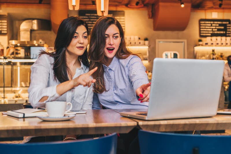 Duas mulheres de negócios novas As meninas com surpresa alegre mostram a mão no tela de computador, olhar das meninas no monitor fotografia de stock Duas mulheres de negócios novas As meninas com surpresa alegre mostram a mão no tela de computador, olhar das meninas no monitor fotografia de stock