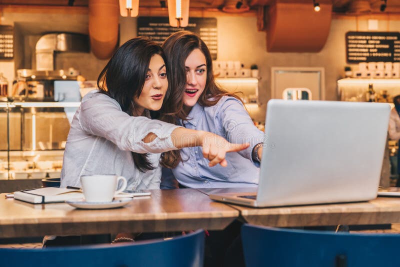 Duas mulheres de negócios novas As meninas com surpresa alegre mostram a mão no tela de computador, olhar das meninas no monitor imagem de stock Duas mulheres de negócios novas As meninas com surpresa alegre mostram a mão no tela de computador, olhar das meninas no monitor imagem de stock