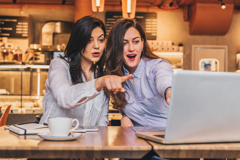 Duas mulheres de negócios novas As meninas com surpresa alegre mostram a mão no tela de computador, olhar das meninas no monitor imagens de stock royalty free Duas mulheres de negócios novas As meninas com surpresa alegre mostram a mão no tela de computador, olhar das meninas no monitor imagens de stock royalty free
