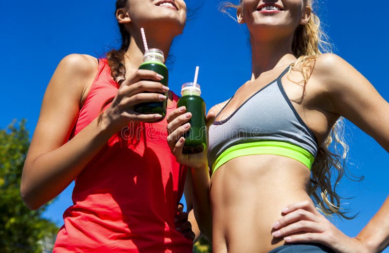 Duas mulheres felizes que bebem o batido vegetal após o runnin da aptidão foto de stock royalty free Duas mulheres felizes que bebem o batido vegetal após o runnin da aptidão foto de stock royalty free