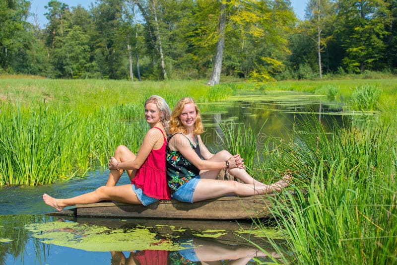 Duas mulheres holandesas novas sentam-se na água na natureza imagens de stock Duas mulheres holandesas novas sentam-se na água na natureza imagens de stock