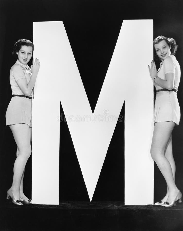 Duas mulheres que levantam com letra enorme M (todas as pessoas descritas não são umas vivas mais longo e nenhuma propriedade exi