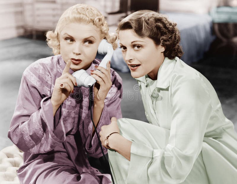 Duas mulheres que sentam-se junto e que escutam no receptor de telefone (todas as pessoas descritas não são nenhum da propriedade imagem de stock royalty free Duas mulheres que sentam-se junto e que escutam no receptor de telefone (todas as pessoas descritas não são nenhum da propriedade imagem de stock royalty free