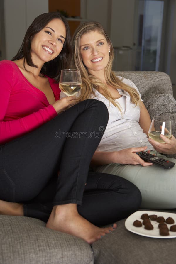 Duas mulheres que sentam-se no vinho bebendo da tevê de Sofa Watching imagem de stock royalty free Duas mulheres que sentam-se no vinho bebendo da tevê de Sofa Watching imagem de stock royalty free