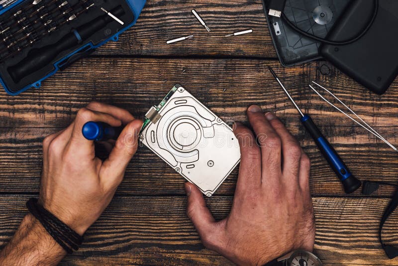 Two Male Hands with Screwdriver Disassemble HDD on Wooden Background. Two Male Hands with Screwdriver Disassemble HDD on Wooden Background