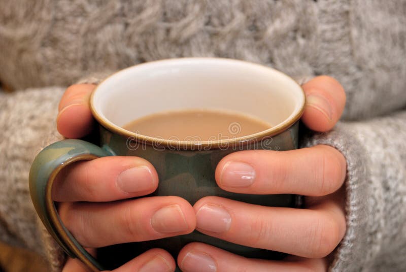 Duas mãos que mantêm-se mornas, guardarando um copo quente do chá ou do café