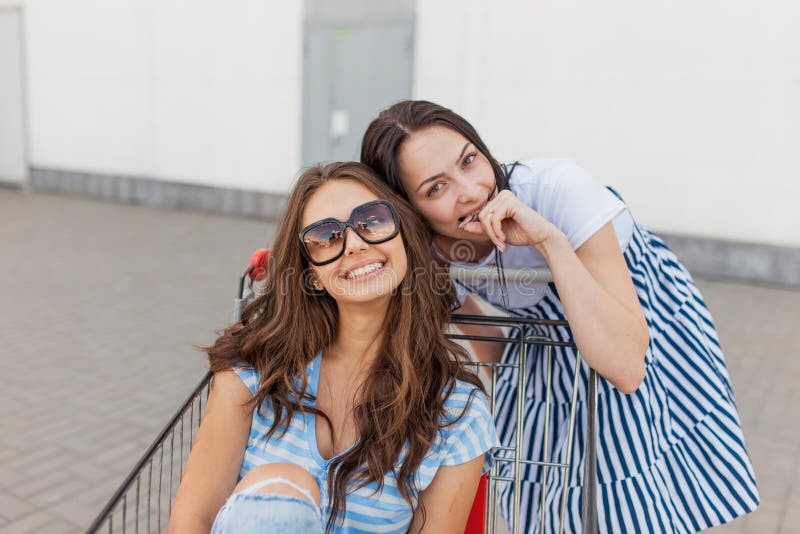 Duas senhoras de cabelo escuro magros de sorriso bonitos, equipamento ocasional vestindo, têm o divertimento com um carro do mant fotografia de stock Duas senhoras de cabelo escuro magros de sorriso bonitos, equipamento ocasional vestindo, têm o divertimento com um carro do mant fotografia de stock
