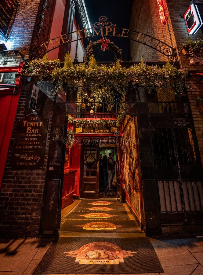 DUBLIN, IRELAND, DECEMBER 24, 2018: Temple Bar historic district, known as cultural quarter with lively nightlife. Nightscene of the bar, full of neon lights and its typically irish pub look, famous, landmark, street, tourism, city, beer, old, urban, attraction, colorful, drink, europe, european, people, travel, building, place, red, music, exterior, destination, entertainment, barrel, capital, corner, food, alcohol, built, lamp, bright, half, cobbled, cross, sign, shamrock