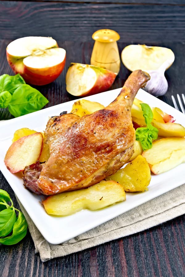 Duck leg with apple and potatoes on dark board.