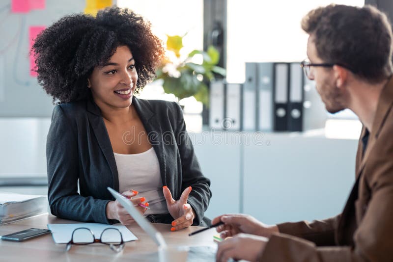 Due aziende multietniche intelligenti che lavorano insieme con il laptop parlando di notizie sul lavoro in ufficio Due aziende multietniche intelligenti che lavorano insieme con il laptop parlando di notizie sul lavoro in ufficio