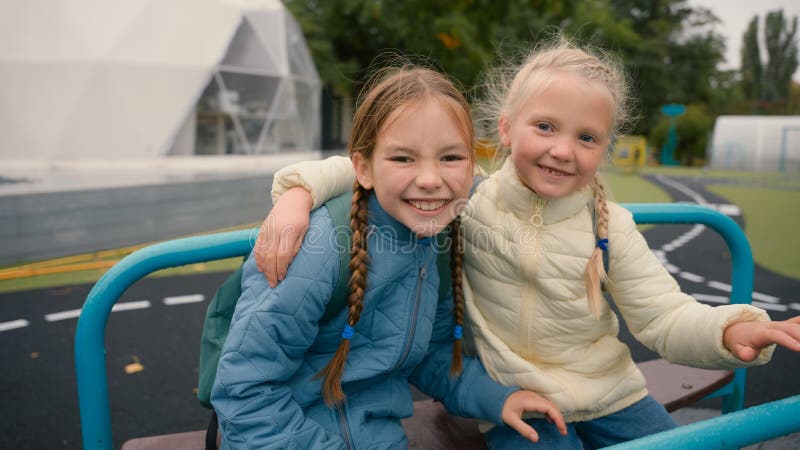 Two little girls friends sisters riding swing laughing smiling joy happiness childhood playground hug fun schoolgirls walk play outside city children classmates kids together school education learning. High quality 4k footage. Two little girls friends sisters riding swing laughing smiling joy happiness childhood playground hug fun schoolgirls walk play outside city children classmates kids together school education learning. High quality 4k footage