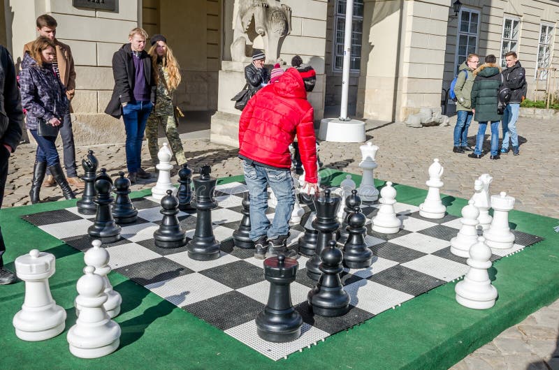 Due bambini che giocano nei pezzi degli scacchi commoventi enormi sul bordo al quadrato del mercato centrale a Leopoli, la gente immagini stock Due bambini che giocano nei pezzi degli scacchi commoventi enormi sul bordo al quadrato del mercato centrale a Leopoli, la gente immagini stock