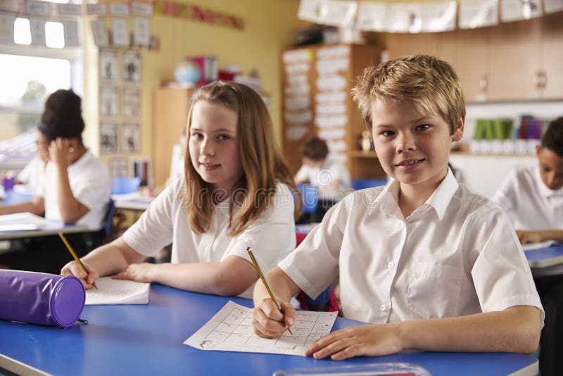 Due bambini in una lezione ad una scuola primaria guardano alla macchina fotografica fotografie stock libere da diritti Due bambini in una lezione ad una scuola primaria guardano alla macchina fotografica fotografie stock libere da diritti