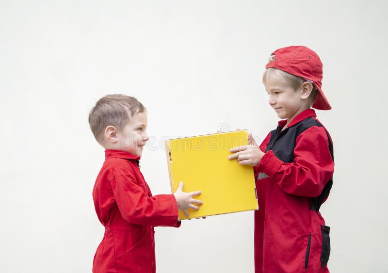 Due bei ragazzi in uniforme rossa che si trovano l'uno di fronte all'altro tengono in mano una scatola gialla sullo sfondo della l immagini stock libere da diritti