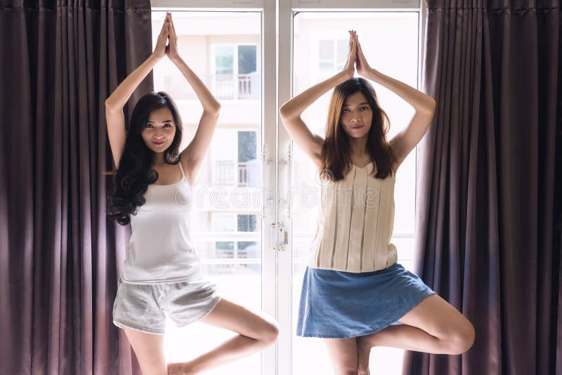 Due bei svegliati sulle ragazze del compagno di camera allungano il corpo dall'esercizio di yoga vicino alla finestra durante l'a immagini stock Due bei svegliati sulle ragazze del compagno di camera allungano il corpo dall'esercizio di yoga vicino alla finestra durante l'a immagini stock