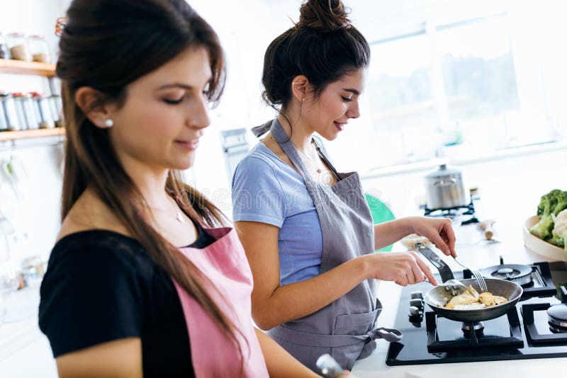 Due belle giovani donne che cucinano petto di pollo nella pentola fotografie stock libere da diritti Due belle giovani donne che cucinano petto di pollo nella pentola fotografie stock libere da diritti