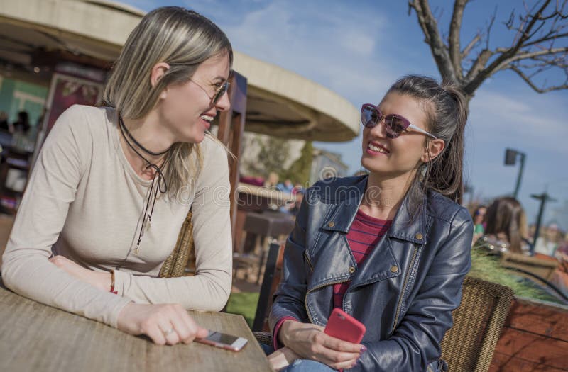 Due belle giovani donne divertendosi all'aperto mentre per mezzo dei loro telefoni cellulari immagini stock Due belle giovani donne divertendosi all'aperto mentre per mezzo dei loro telefoni cellulari immagini stock