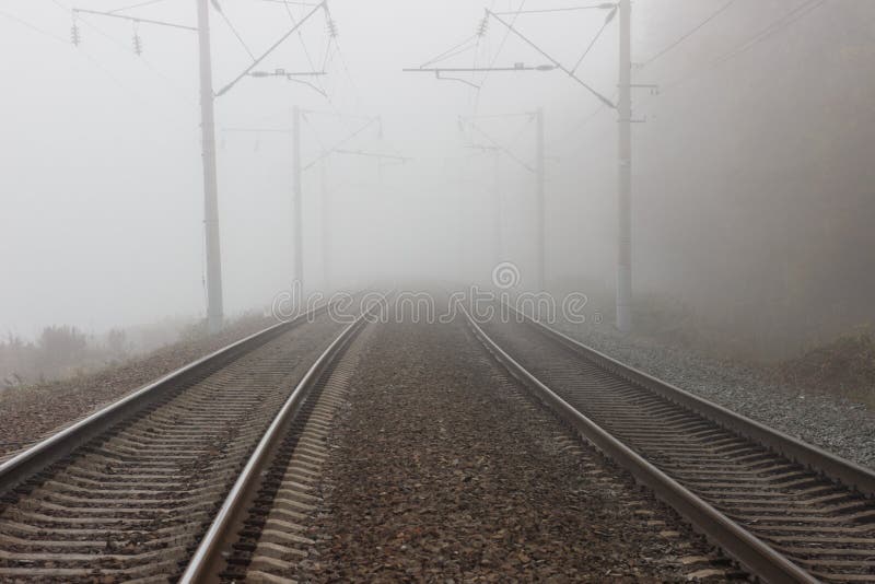 Due binari paralleli della ferrovia che vanno nella distanza tra nebbia e sospensione