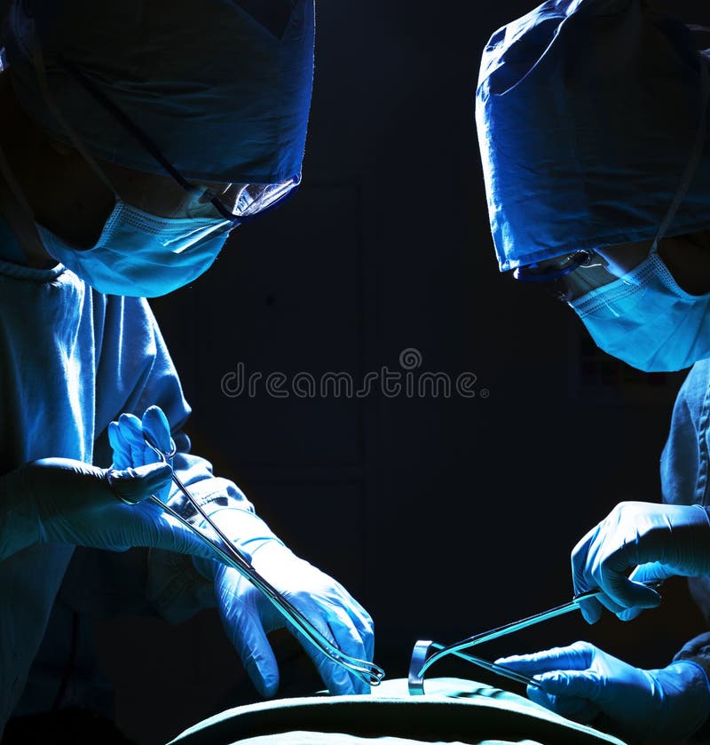 Due chirurghi che guardano giù, lavoranti e tenenti attrezzatura chirurgica con il paziente che si trova sul tavolo operatorio immagine stock libera da diritti Due chirurghi che guardano giù, lavoranti e tenenti attrezzatura chirurgica con il paziente che si trova sul tavolo operatorio immagine stock libera da diritti