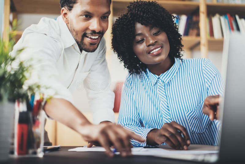 Due colleghe giovani che lavorano insieme in un ufficio moderno Soci commerciali neri che discutono nuovo progetto startup fotografia stock Due colleghe giovani che lavorano insieme in un ufficio moderno Soci commerciali neri che discutono nuovo progetto startup fotografia stock