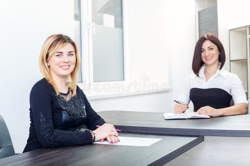Due donne che si siedono ad una tavola nell'ufficio Biondo e castana sull'intervista di lavoro, o sulla riunione immagine stock libera da diritti Due donne che si siedono ad una tavola nell'ufficio Biondo e castana sull'intervista di lavoro, o sulla riunione immagine stock libera da diritti