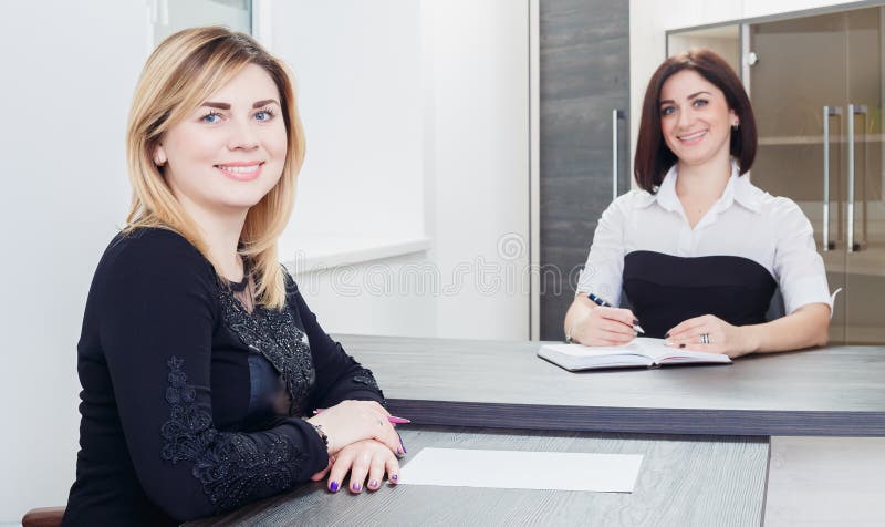 Due donne che si siedono ad una tavola nell'ufficio Biondo e castana sull'intervista di lavoro, o sulla riunione immagine stock libera da diritti Due donne che si siedono ad una tavola nell'ufficio Biondo e castana sull'intervista di lavoro, o sulla riunione immagine stock libera da diritti