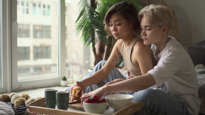 Due donne lesbiche che baciano e mangiano croissant mentre fanno colazione a letto a casa spbd. archivi video