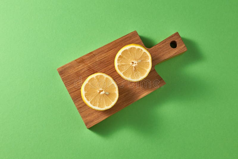 Due fette rotonde di limone giallo maturo su un bordo di legno di taglio su un fondo verde Vista superiore fotografia stock libera da diritti Due fette rotonde di limone giallo maturo su un bordo di legno di taglio su un fondo verde Vista superiore fotografia stock libera da diritti