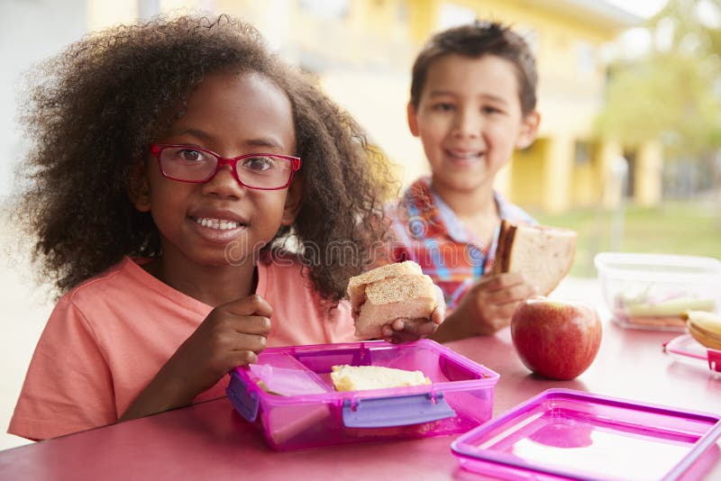 Due giovani bambini della scuola che mangiano insieme i loro pranzi imballati