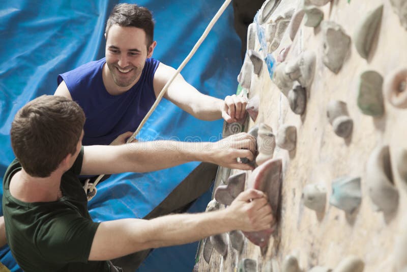 Due giovani che sorridono ad a vicenda e che scalano in una palestra rampicante dell'interno immagine stock Due giovani che sorridono ad a vicenda e che scalano in una palestra rampicante dell'interno immagine stock