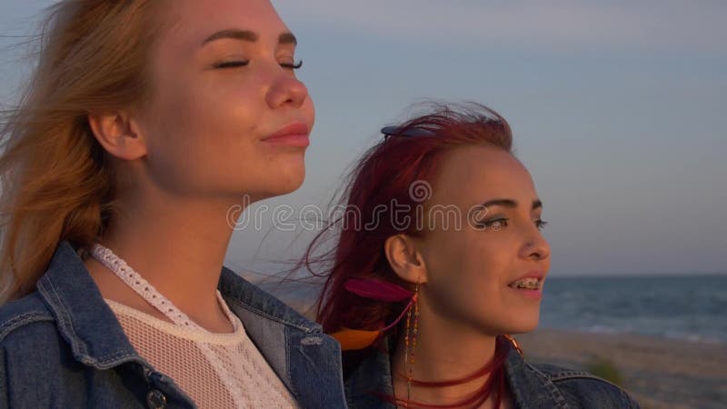 Due giovani donne nei raggi delicati del tramonto sui precedenti della spuma del mare