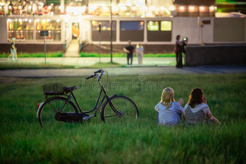 Due giovani donne si rilassano sull'erba e una bicicletta godendosi il tempo libero sul fiume wisla, lungo le rive del krakow, ambientando la sera. serata classica a krakow
