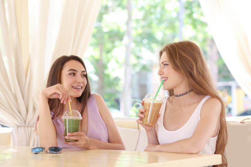 Due giovani signore piacevoli che bevono frullato immagini stock Due giovani signore piacevoli che bevono frullato immagini stock