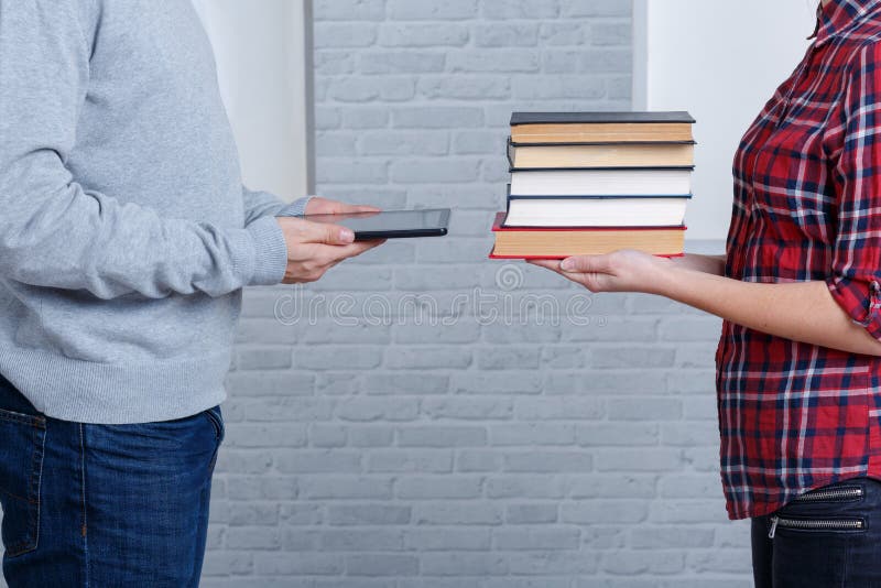 Due giovani stanno di fronte a vicenda ed alle tenute il mucchio dei libri ed alla compressa moderna fotografie stock libere da diritti Due giovani stanno di fronte a vicenda ed alle tenute il mucchio dei libri ed alla compressa moderna fotografie stock libere da diritti