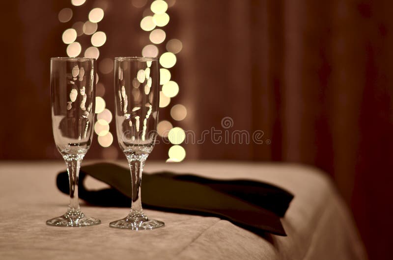 Due goblet di vetro sul bordo del letto nella camera da letto, accanto a un uomo legato tra le luci che imitano bolle di champagn immagine stock libera da diritti Due goblet di vetro sul bordo del letto nella camera da letto, accanto a un uomo legato tra le luci che imitano bolle di champagn immagine stock libera da diritti
