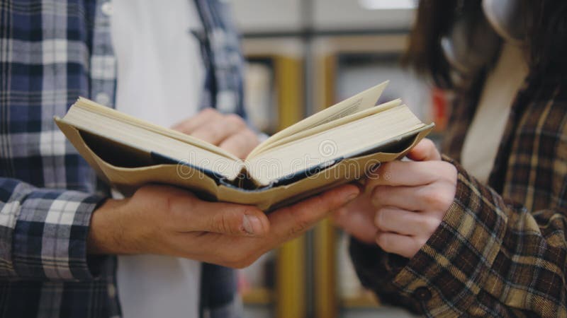 Due individui sfogliano un libro in una biblioteca esplorando diverse pagine durante un attento momento di scoperta e archivi video